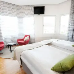 Ett modernt hotellrum med två sängar, röda fåtöljer och utsikt över en plaza i Borås.