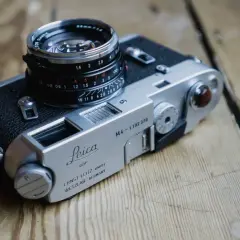 A classic Leica M4-P camera with a Summicron lens sits on a wooden surface.