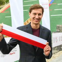 Uśmiechnięty mężczyzna trzyma biało-czerwoną wstęgę. Czy to symbol otwarcia obiektu, który ma ile lat stoch?