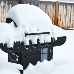 En snötäckt gasolgrill under tak, redo för sommarens grillkvällar trots vinterns kyla.