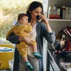 Kobieta z dzieckiem na rękach pije kawę. Czy kawe inke moga pic dzieci? To pytanie nurtuje wielu rodziców.