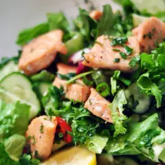 Pyszna sałatka z łososiem, świeżymi ogórkami, sałatą i ziołami, skropiona cytryną.
