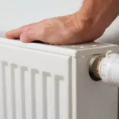Mano sobre radiador blanco, ajustando el termostato. Es hora de decidir cuándo poner la calefacción para estar cómodo.