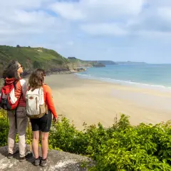 Deux randonneuses contemplent la plage de sable fin et la mer bleue, un paysage typique du GR34 à Saint-Brieuc.
