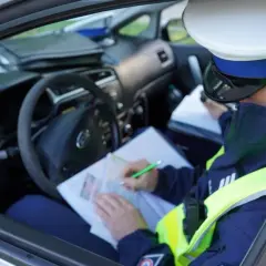 Policjant w radiowozie spisuje mandat za jazdę bez kasku.