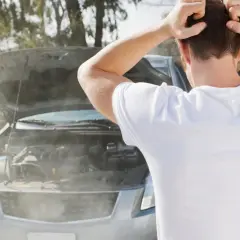 Hombre frustrado mira cómo sale humo blanco del motor de su coche averiado.