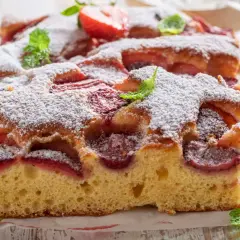 Puszyste ciasto z truskawkami, posypane cukrem pudrem i ozdobione listkami mięty. Wygląda jak najlepsze ciasto z truskawkami, jakie można sobie wymarzyć!