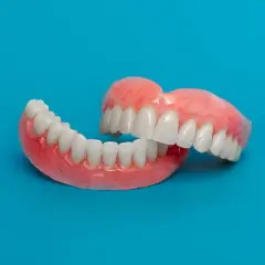 Un paio di protesi dentarie, con denti bianchi e gengive rosa, su sfondo blu. Soluzione per denti mobili.