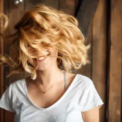 Uśmiechnięta dziewczyna z burzą włosów w odcieniu maślany blond, które wirują wokół jej twarzy.