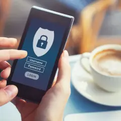 Dłoń trzyma smartfon z ekranem logowania do bankowości internetowej. Widoczne pole na hasło i ikonka kłódki symbolizują bezpieczeństwo.