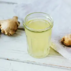 Imbir i napar z niego to naturalne domowe sposoby na wymioty. Napój w szklance, świeży imbir i anyż na drewnianym tle.