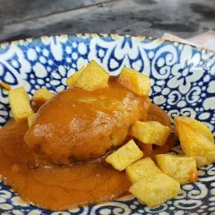 Rollo de bonito asturiano bañado en salsa, acompañado de patatas fritas en dados, servido en un plato azul y blanco.