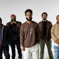 Fünf Männer stehen vor weißem Hintergrund. Einer trägt ein **butcher brown** Langarmshirt mit einem Hirschgeweih-Symbol.