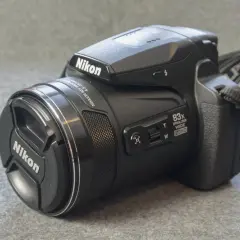 A black Nikon P90 camera with an 83x optical zoom lens sits on a textured gray surface.