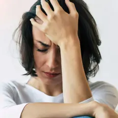 En kvinna med handen mot pannan, ansiktet nedåt, visar tydliga tecken på depression och dess fysiska symptom som huvudvärk och utmattning.