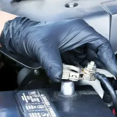 Ręka w czarnej rękawiczce dokręca śrubę na klemie akumulatora samochodowego.
