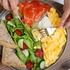 Assiette colorée avec saumon fumé, œufs brouillés, salade verte, tomates séchées, concombre et pain complet. Un repas protéiné parfait pour bien commencer la journée.