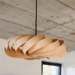 Drewniana lampka DIY o spiralnym kształcie, zawieszona pod betonowym sufitem.