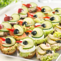 Kolorowe kanapki na talerzu, idealne na pan kanapka catering. Różne dodatki: łosoś, jajko, ogórek, oliwki, winogrona.