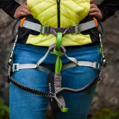 Osoba w kamizelce i jeansach ma na sobie sprzęt do via ferrata, w tym lonżę z karabinkami.