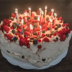 Pyszne ciasto urodzinowe z bitą śmietaną, truskawkami, malinami, borówkami i porzeczkami, ozdobione płonącymi świeczkami.