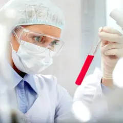 Naukowczyni w okularach i masce bada probówkę z czerwonym płynem. Czy to prokalcytonina, co to za wskaźnik?