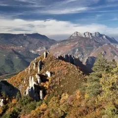 Vue panoramique des gorges de la Roanne en automne. Un sentier de randonnée serpente à travers des crêtes rocheuses et des forêts aux couleurs flamboyantes.