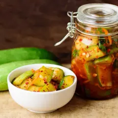 Słoik i miseczka z pikantnymi ogórkami z papryką chili, obok świeże ogórki.