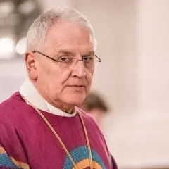 Bischof Heinrich Timmervers trägt ein violettes Messgewand mit bunten Streifen. Er blickt ernst in die Kamera.