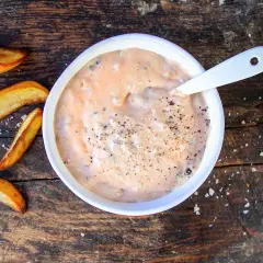 En skål med krämig hamburgerdressing, perfekt för ditt nästa hamburgerdressing recept. Serveras med klyftpotatis på en träbakgrund.