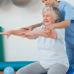 Terapeuta ayuda a una mujer mayor con ejercicios de movilidad sentada en una pelota de ejercicio.