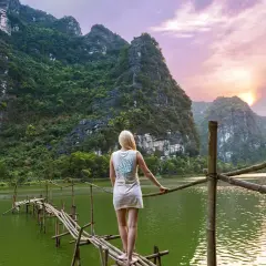 Frau auf Bambusbrücke in Vietnam, umgeben von Karstbergen und einem See. Tolle Reise-Hacks für unvergessliche Momente.