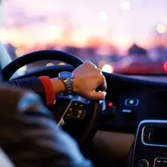 Mano al volante, orologio elegante, tramonto sfocato. Una guida esperta affronta la sera con sicurezza.