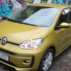 Żółty Volkswagen up! zaparkowany pod kolorowym graffiti.