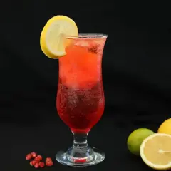 Orzeźwiający drink z sokiem z granatu, ozdobiony plasterkiem cytryny. Obok leżą owoce granatu, cytryny i limonka.