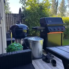En Weber kolgrill bäst i test står redo för sommarens grillkvällar bredvid en gasolgrill. Trädgårdsmöbler och en fin gräsmatta skapar en härlig atmosfär.