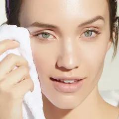 Mujer con toalla blanca limpiando su rostro, evitando el maquillaje cuarteado.