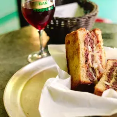 Un delicioso patty melt con carne jugosa y cebolla caramelizada, servido en pan tostado, junto a una copa de vino tinto.