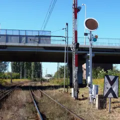 Tarcza ostrzegawcza przy torach kolejowych pod wiaduktem. Sygnalizacja świetlna i znak krzyżowy informują o zbliżającym się niebezpieczeństwie.
