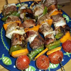 Brochetas de solomillo con pimientos verdes, cebolla y tomate, servidas en un plato azul con dibujos de peces.
