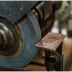 Zbliżenie na kamień szlifierski i metalowy element, pokazujące różne rodzaje kamieni szlifierskich w akcji.