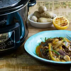 En läcker slow cooker recept med mört kött, citron och rosmarin på en blå tallrik bredvid en Crock-Pot.