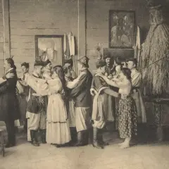 Grupa ludzi w strojach ludowych tańczy w pomieszczeniu, obok słomiana postać.