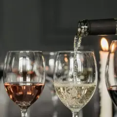 Degustacja wina w blasku świec. Nalewanie białego wina do kieliszka, obok różowe i czerwone wino.