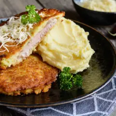Złocisty sznycel wieprzowy z ziemniakami puree i startym serem, udekorowany natką pietruszki. Pyszny obiad gotowy do podania.