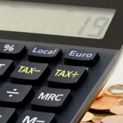 Kalkulator z klawiszami "TAX+", "TAX-" i "Euro" obok stosu monet. Czas na rozliczenie działalności gospodarczej do kiedy?