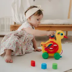 Mała dziewczynka w kwiecistej sukience bawi się żółtym pajacykiem zabawką na kółkach.