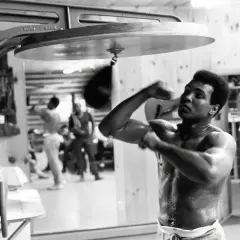 Muhammad Ali trains with a speed bag, sweat glistening on his skin, a testament to the dedication behind his many achievements.