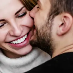 Uśmiechnięta kobieta, której mężczyzna szepcze do ucha. Idealny **wodnik horoskop miłosny** dla zakochanych.