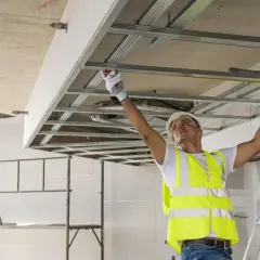 Obrero mide estructura de techo falso. Para saber si un muro es de carga, observa su grosor y si soporta peso.